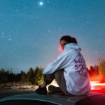 una ragazza guarda il cielo stellato sul tettuccio di una macchina